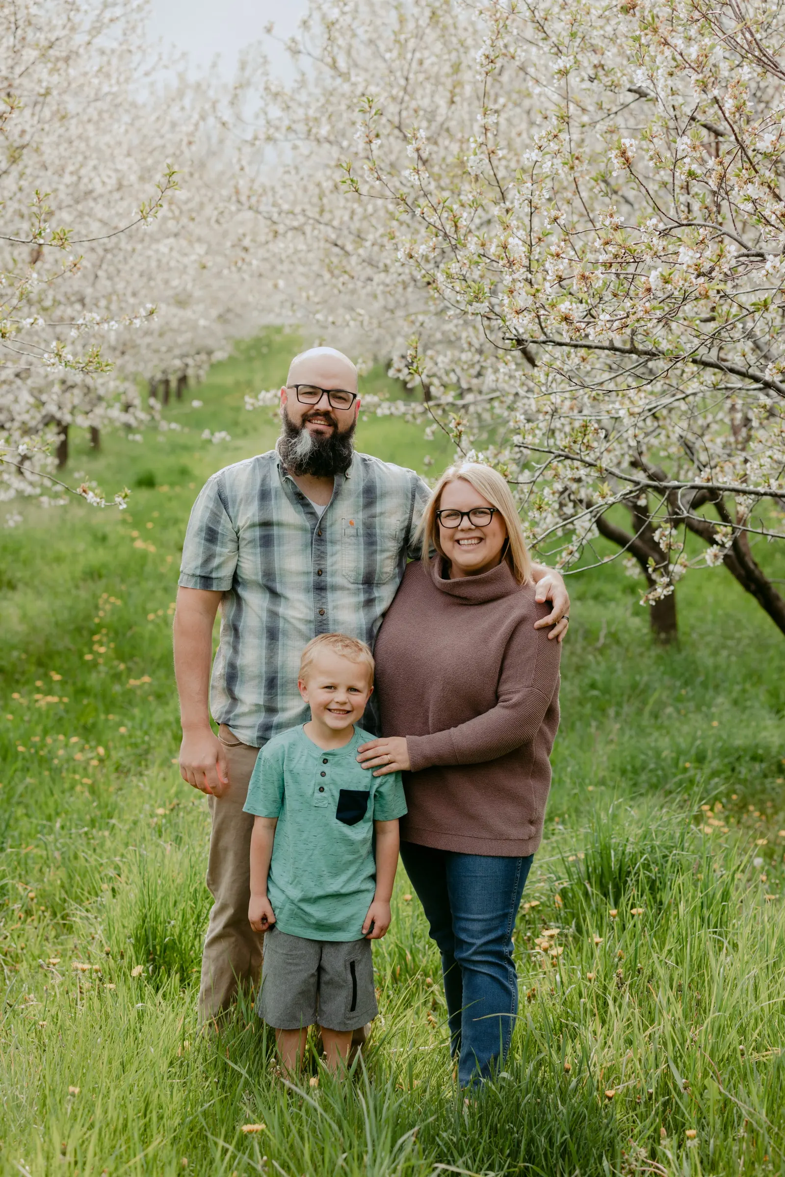 A family of three standing among blooming cherry trees on Old Mission Peninsula
